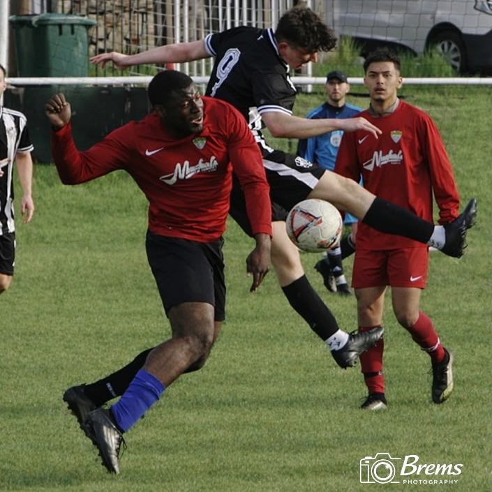 Footballers playing football with the ball in the air during a tackle