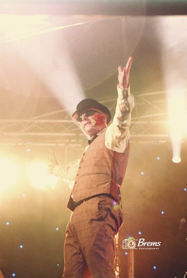 A man at a music concert wearing a black bower hat with a red rose in his mouth