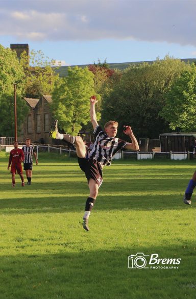 A footballer at a football match with his leg doing a high kick