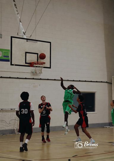 A group of young people with the ball in the air taking a shot at a basket ball match