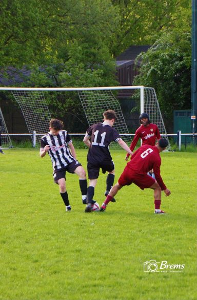 Football players at a football match passing the ball with the goal nets in the background